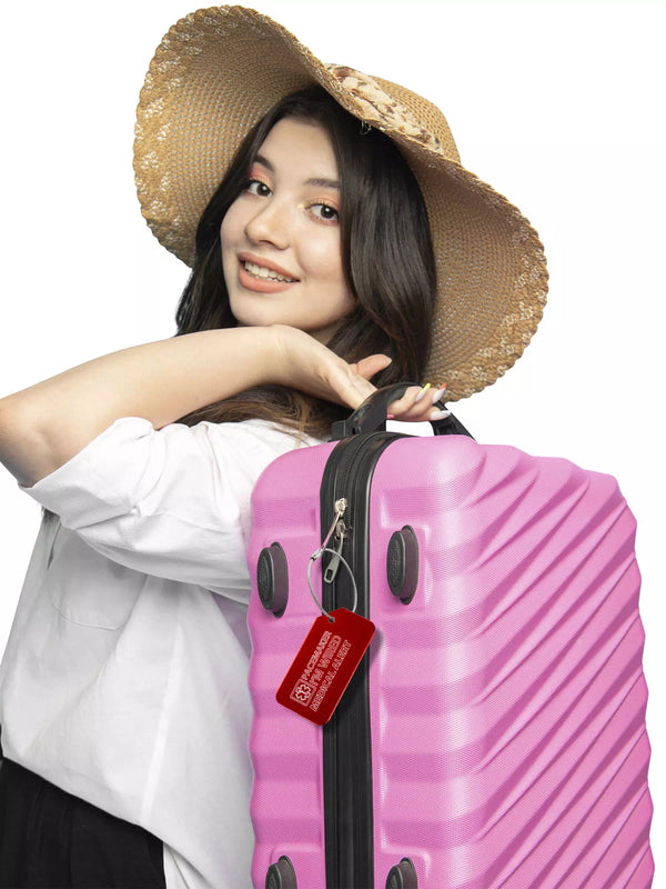 Woman wearing a hat and holding a pink suitcase with a red medical luggage tag attached.