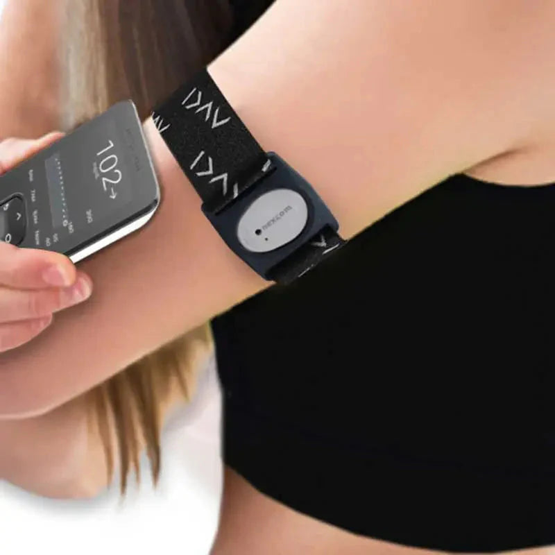 Person wearing a Dexcom G7 armband with a continuous glucose monitor attached, holding a smartphone displaying glucose level data, representing a wearable device for diabetes management. Image